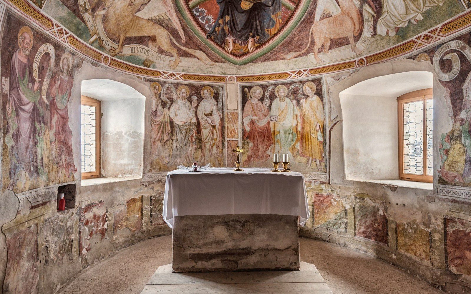 Faded medieval frescoes of saints cover the apse walls above a stone altar